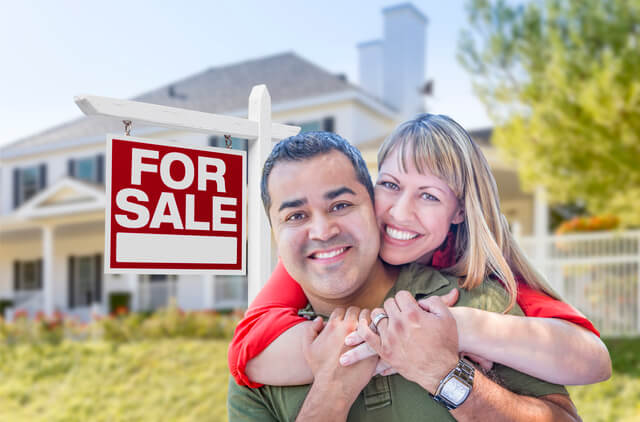 Happy couple selling their home with for sale sign in yard.